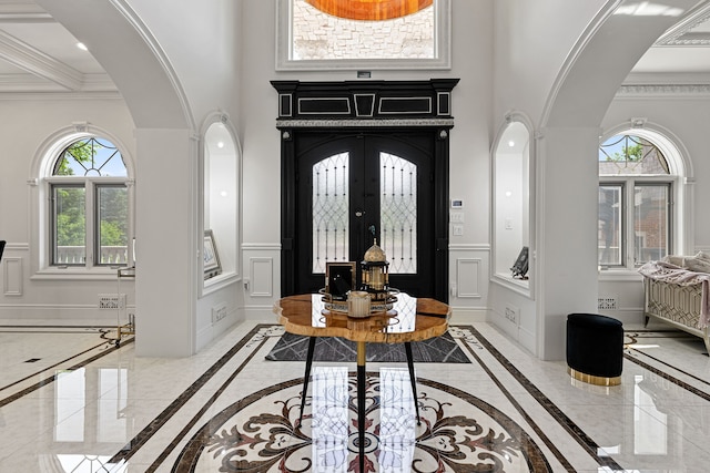 foyer featuring plenty of natural light, ornamental molding, a towering ceiling, and french doors