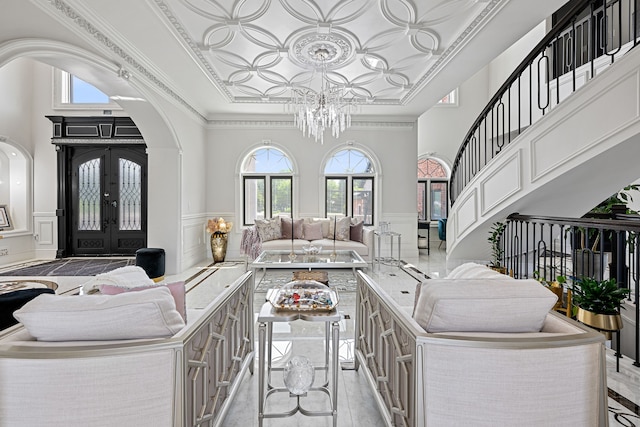 living room featuring french doors, light hardwood / wood-style flooring, crown molding, a towering ceiling, and a chandelier