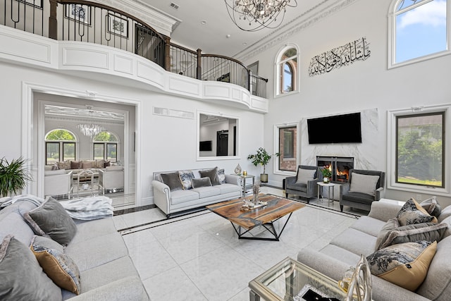 living room featuring a high end fireplace, a towering ceiling, ornamental molding, light tile patterned floors, and a chandelier