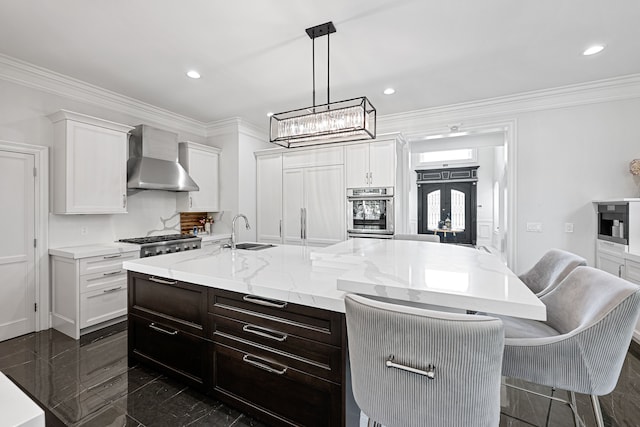 kitchen featuring a center island with sink, white cabinets, wall chimney range hood, sink, and hanging light fixtures