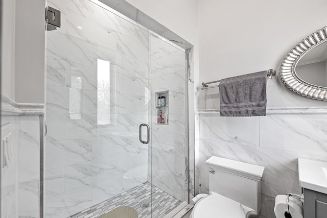 bathroom with a shower with door, vanity, tile walls, and toilet