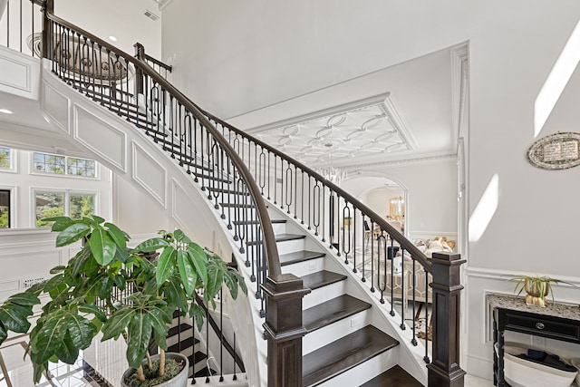 staircase featuring a towering ceiling, ornamental molding, and a notable chandelier