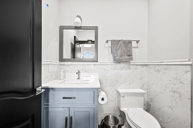 bathroom featuring vanity, toilet, and tile walls