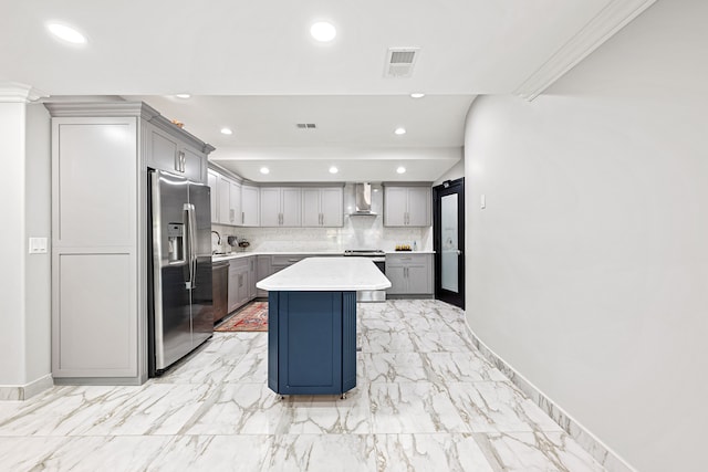 kitchen featuring a center island, wall chimney range hood, backsplash, gray cabinets, and appliances with stainless steel finishes