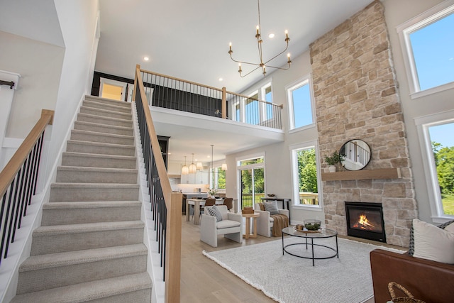 living room featuring a notable chandelier, light wood-type flooring, a fireplace, and a high ceiling