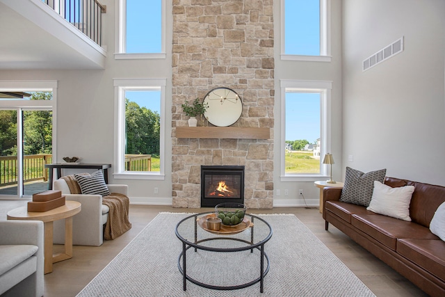 living room featuring a towering ceiling, a stone fireplace, and a healthy amount of sunlight