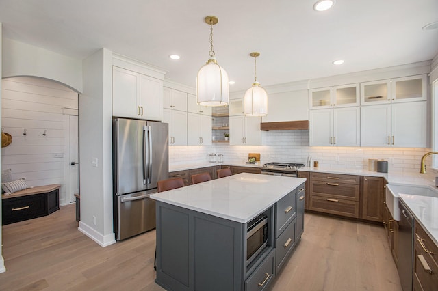 kitchen featuring appliances with stainless steel finishes, light stone counters, white cabinets, a center island, and light hardwood / wood-style floors