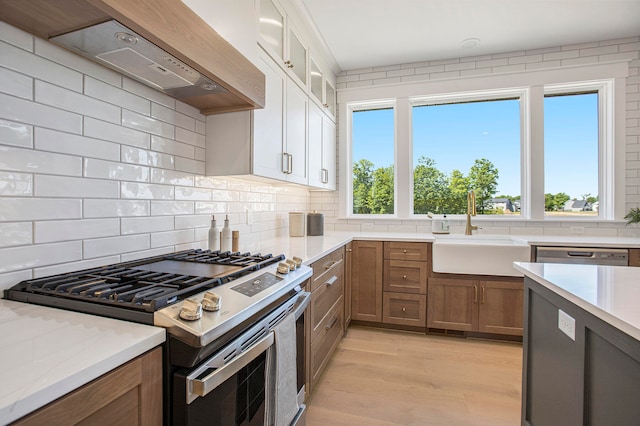 kitchen with sink, wall chimney exhaust hood, stainless steel appliances, plenty of natural light, and white cabinets