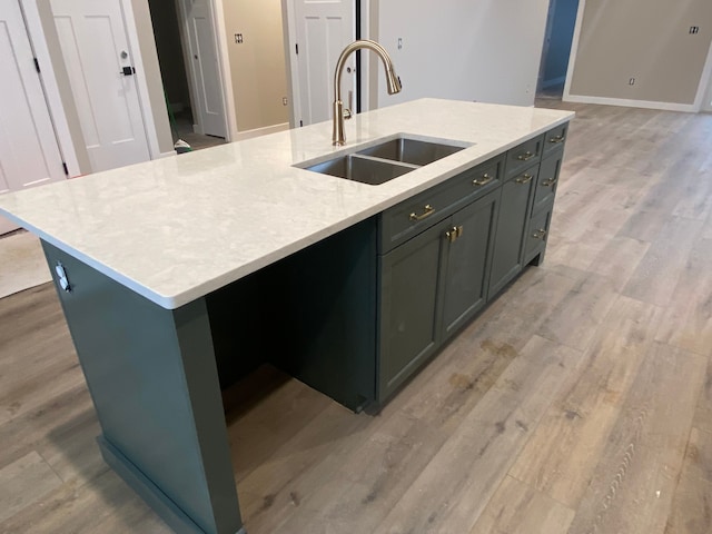 kitchen featuring light stone countertops, a kitchen island with sink, sink, and light hardwood / wood-style flooring