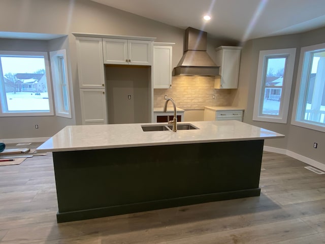 kitchen with premium range hood, white cabinetry, a center island with sink, and tasteful backsplash