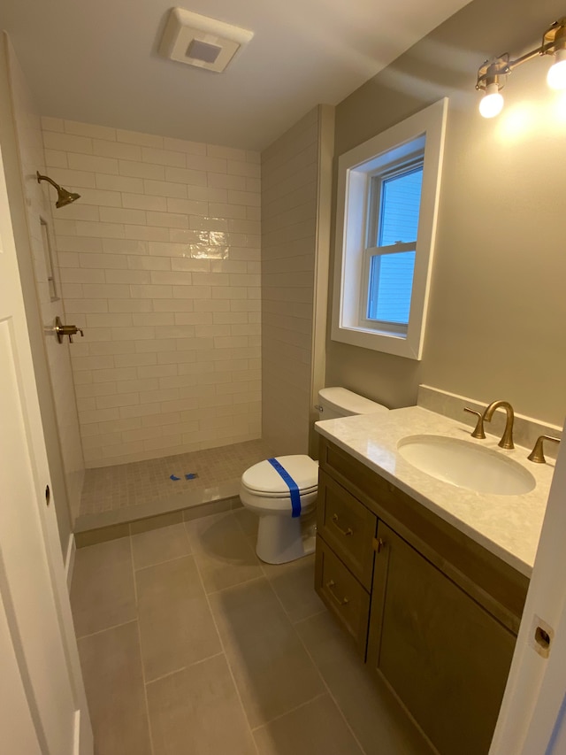 bathroom featuring vanity, toilet, tiled shower, and tile patterned flooring