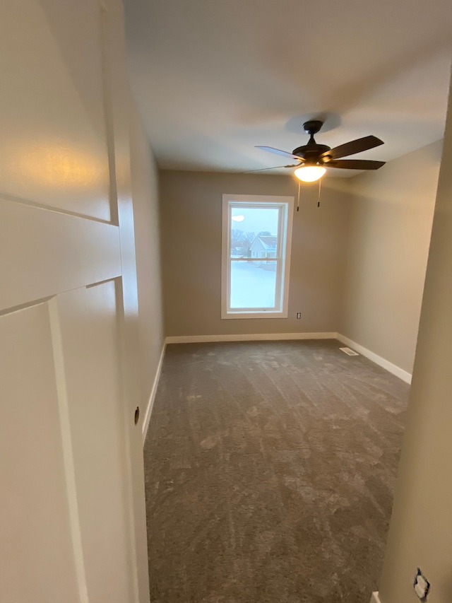 empty room featuring ceiling fan and dark carpet