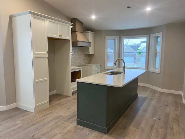 kitchen featuring sink, light hardwood / wood-style flooring, a center island with sink, custom range hood, and white cabinets