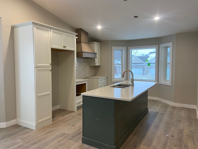 kitchen featuring custom range hood, sink, tasteful backsplash, white cabinetry, and a center island with sink