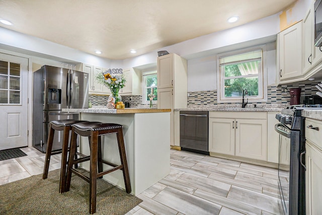 kitchen with a breakfast bar, sink, decorative backsplash, white cabinetry, and stainless steel appliances