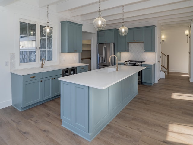 kitchen with beam ceiling, sink, stainless steel appliances, a center island with sink, and light wood-type flooring