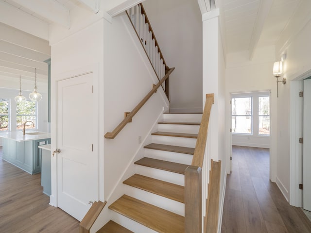 staircase with beam ceiling, a wealth of natural light, and wood-type flooring