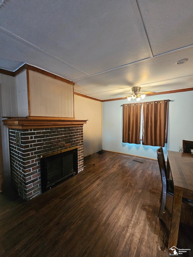 living room with ceiling fan, dark wood-type flooring, a brick fireplace, wood walls, and a textured ceiling