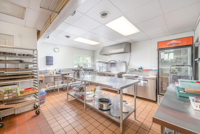 18564 200th, Tustin, MI 49688 - kitchen with stainless steel counters, a paneled ceiling, wall chimney range hood, light tile patterned flooring, and range