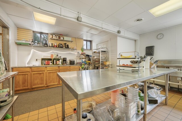 18564 200th, Tustin, MI 49688 - kitchen featuring stainless steel countertops, brown cabinets, a paneled ceiling, healthy amount of natural light, and light tile patterned floors