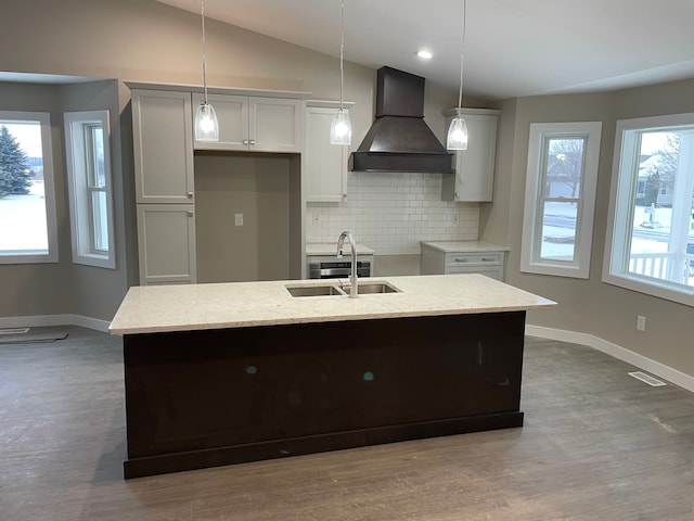 kitchen with custom range hood, sink, decorative light fixtures, a center island with sink, and decorative backsplash