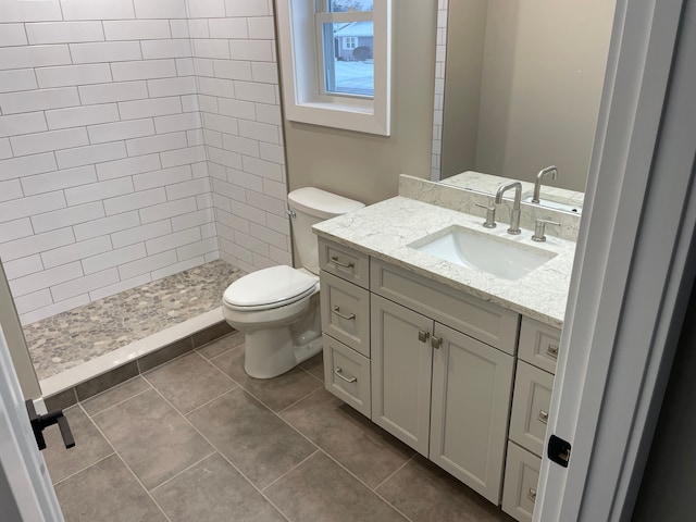 bathroom with vanity, tile patterned flooring, toilet, and a tile shower