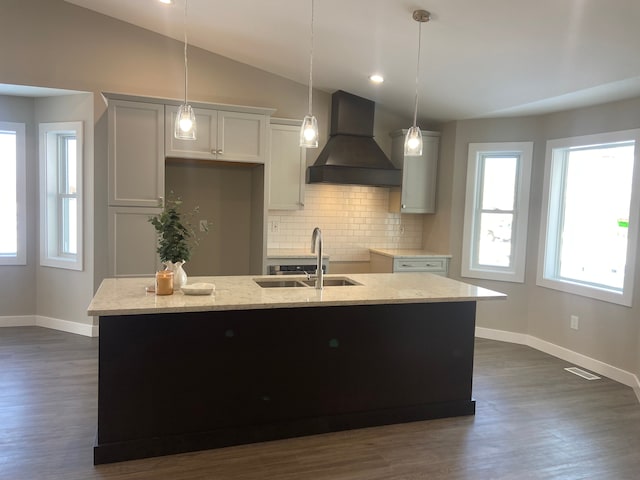 kitchen featuring pendant lighting, sink, a kitchen island with sink, light stone countertops, and custom range hood