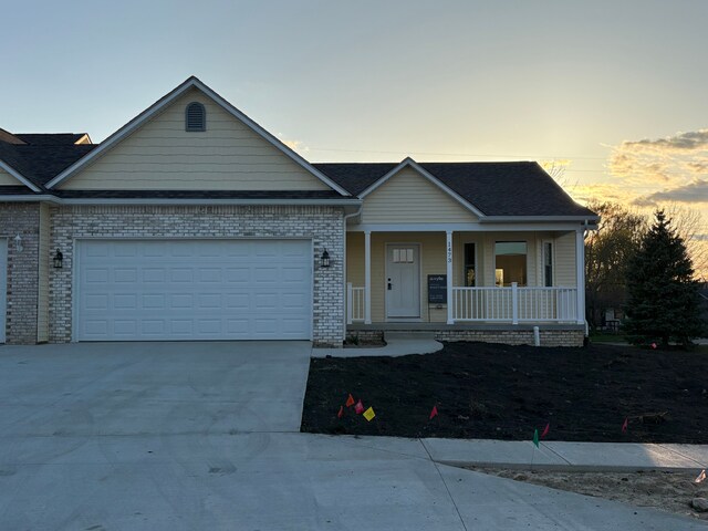 1473 Mallard Cir, Owosso, MI 48867 - view of front of house with brick siding, a porch, concrete driveway, and an attached garage