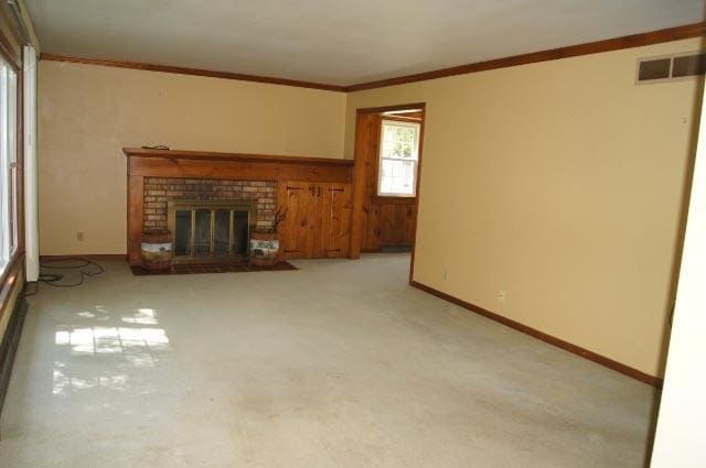 unfurnished living room with light carpet, crown molding, and a brick fireplace