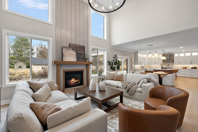 living room with light hardwood / wood-style floors, a towering ceiling, ornamental molding, and a chandelier