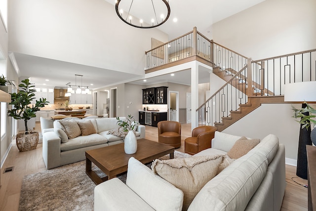 living room with a chandelier, a high ceiling, light wood-type flooring, and indoor bar