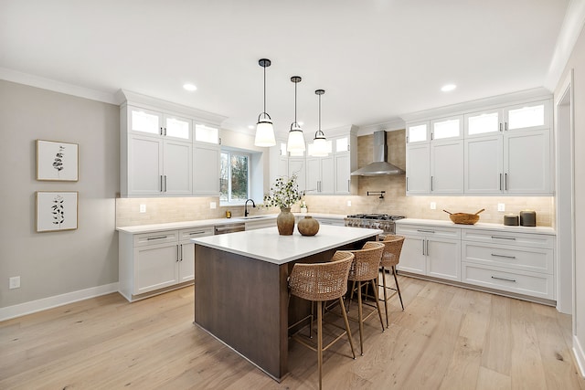 kitchen with white cabinets, sink, a center island, and wall chimney range hood