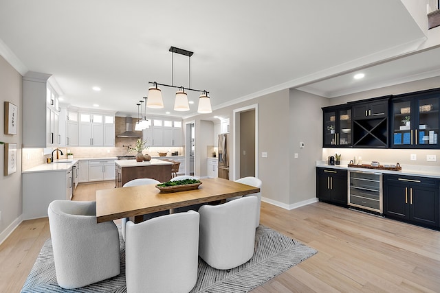 dining area featuring ornamental molding, sink, beverage cooler, and light wood-type flooring