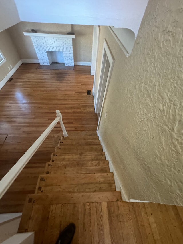 staircase with hardwood / wood-style floors and a brick fireplace