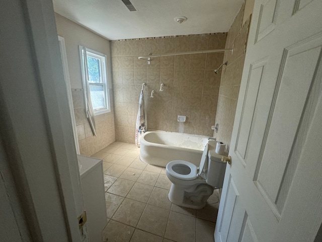 bathroom with tile patterned flooring, tiled shower / bath, toilet, and tile walls