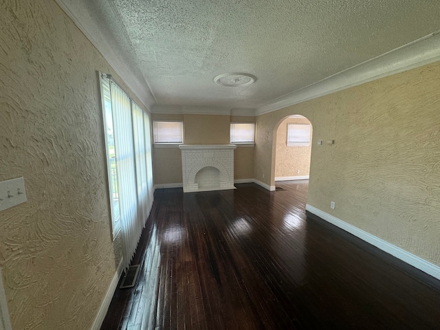 unfurnished living room featuring ornamental molding, dark wood-type flooring, a textured ceiling, and a brick fireplace