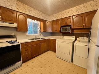 kitchen with a textured ceiling, white appliances, washer and clothes dryer, sink, and exhaust hood