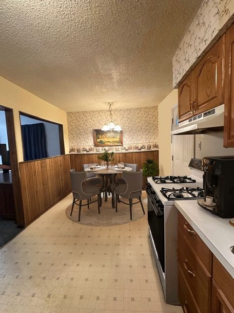 kitchen with wooden walls, hanging light fixtures, a textured ceiling, and white gas range oven