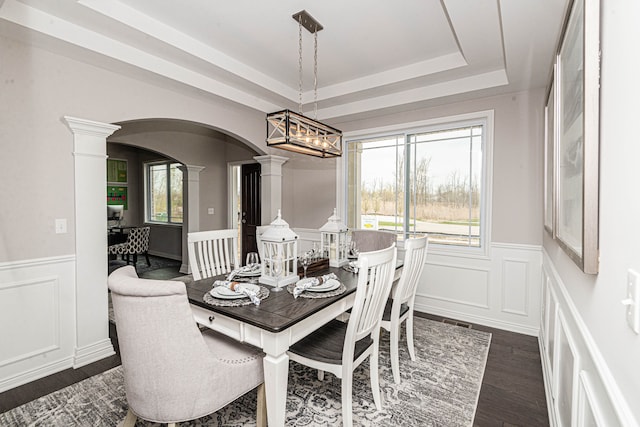 dining room featuring a raised ceiling, ornate columns, dark wood-type flooring, and an inviting chandelier