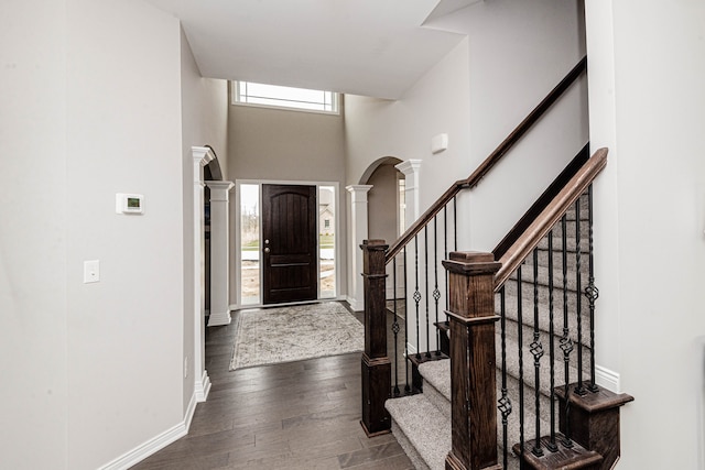 foyer entrance with ornate columns, a towering ceiling, and dark hardwood / wood-style floors