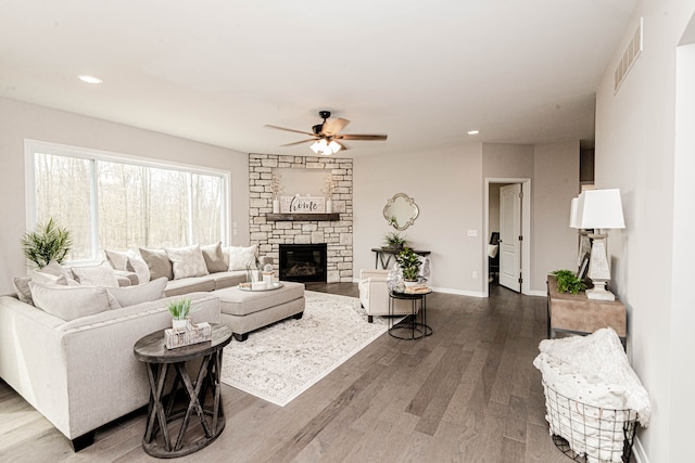 living room featuring dark hardwood / wood-style flooring, a stone fireplace, and ceiling fan