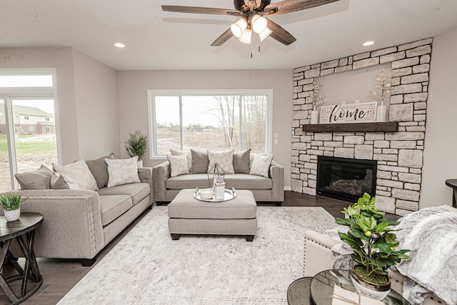 living room featuring a stone fireplace, ceiling fan, and dark wood-type flooring