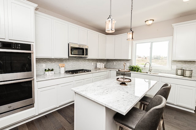 kitchen with a center island, dark hardwood / wood-style floors, light stone countertops, appliances with stainless steel finishes, and white cabinetry