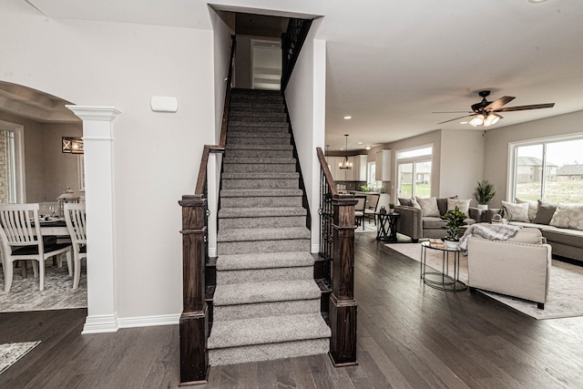 stairway with hardwood / wood-style flooring, ceiling fan with notable chandelier, and ornate columns