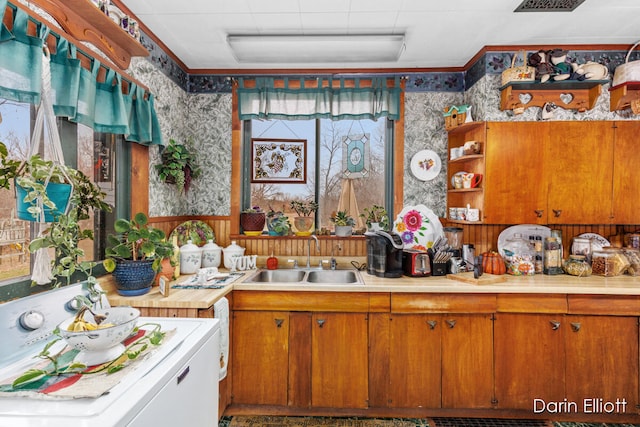 kitchen featuring light countertops, a sink, open shelves, and wallpapered walls