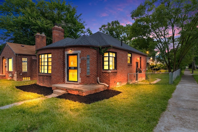 back house at dusk featuring a lawn