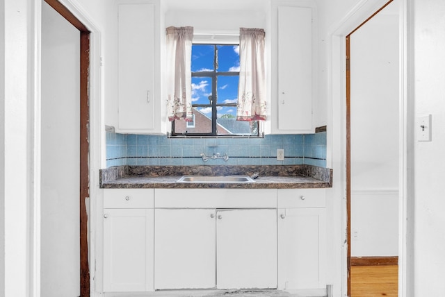 kitchen featuring tasteful backsplash, white cabinetry, hardwood / wood-style flooring, and sink