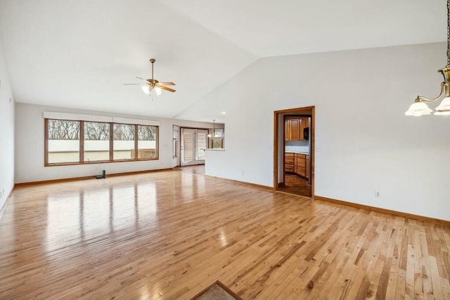 unfurnished living room with ceiling fan with notable chandelier, high vaulted ceiling, and light wood-type flooring