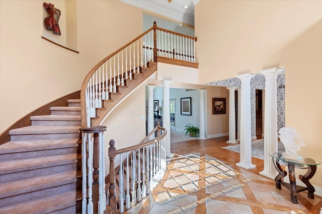 stairs featuring a high ceiling, decorative columns, and crown molding