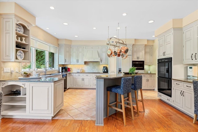 kitchen featuring backsplash, custom range hood, sink, black appliances, and white cabinets